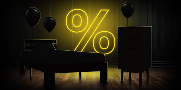 Cama preta e cómoda com balões pretos em frente a um sinal de percentagem amarelo brilhante num piso de madeira escura.