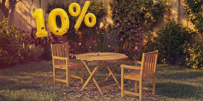  Mesa de jantar de madeira para exterior com duas cadeiras a condizer num ambiente de jardim, decorada com confetes cor-de-rosa e balões dourados com «10% de desconto», destacando uma promoção sazonal de mobiliário de jantar para exterior.