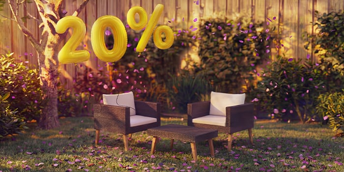  Cadeirões lounge de rattan para exterior com almofadas e uma pequena mesa num ambiente de jardim, decorados com confetes cor-de-rosa e balões dourados com «20% de desconto», destacando promoções sazonais em mobiliário lounge de jardim.