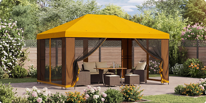 Caramanchão de jardim amarelo com cortinas em rede, que abriga um conjunto de exterior com mesa num pátio, rodeado por plantas floridas num jardim ensolarado.